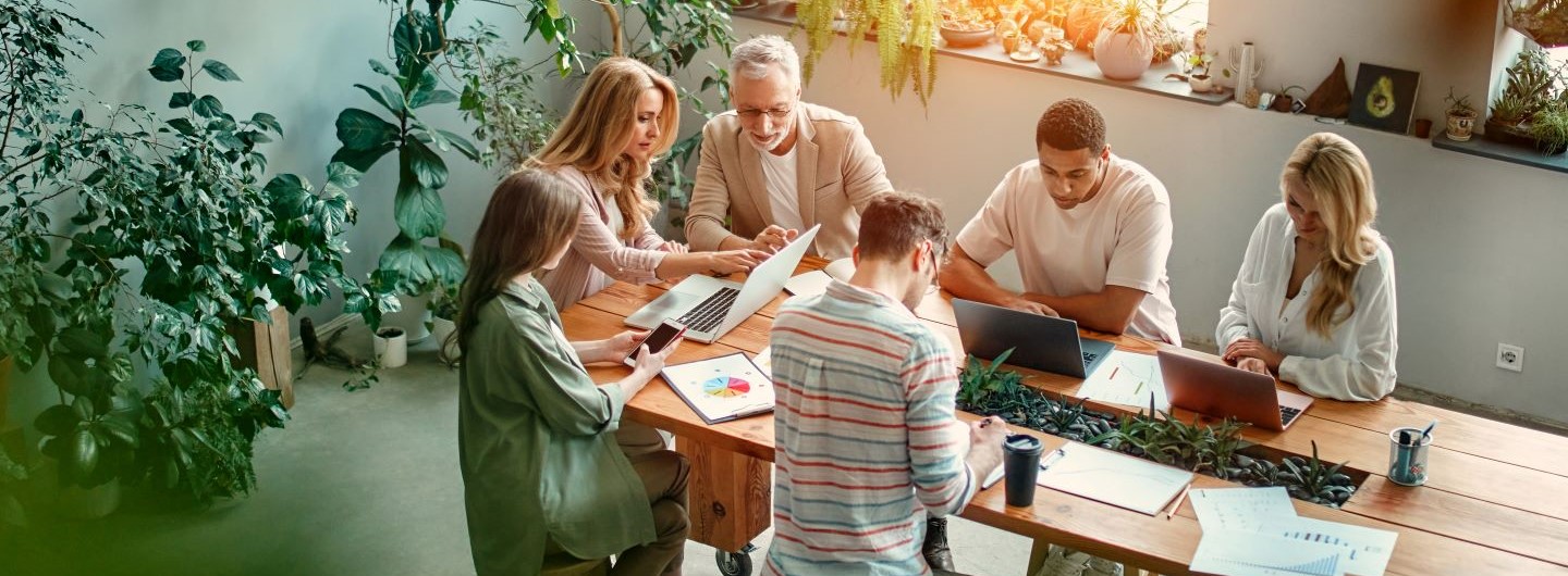 Gruppe von Kollegen arbeiten an einem Tisch kreativ an Laptops