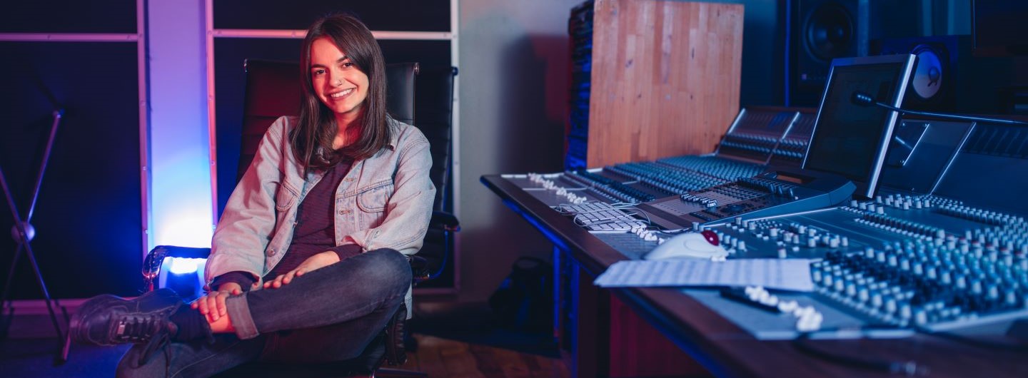 Digitale Musikproduktion Weiterbildung: Eine junge Musikproduzentin sitzt lächelnd am Mischpult