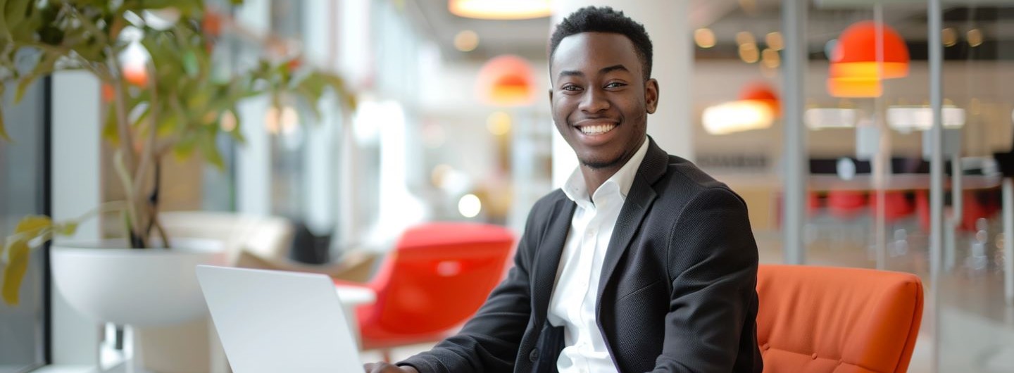 Information Systems Management Studium: ein junger Information Systems Manager sitzt an seinem Laptop in einem modernen Büro und lächelt in die Kamera