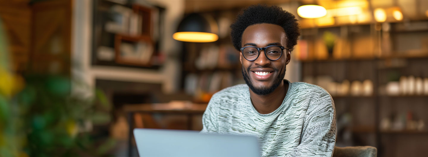 IT Studium: ein junger Administrator sitzt vor seinem Laptop und lächelt in die Kamera