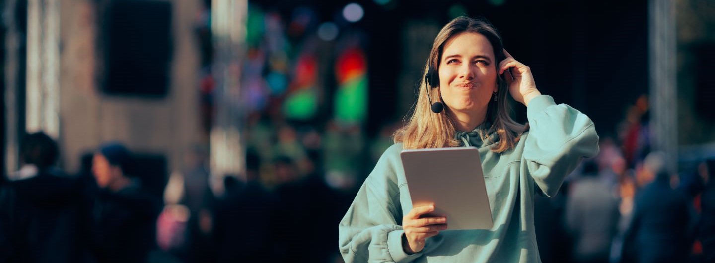 Musikmanagerin steht mit Headset und Tablet vor Bühne auf Festival