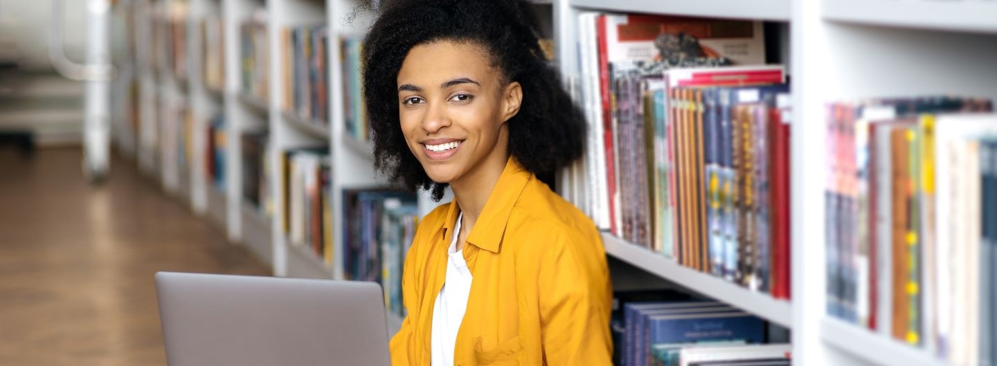 Philologie Studium Junge Frau sitzt mit Laptop vor Bücherregal