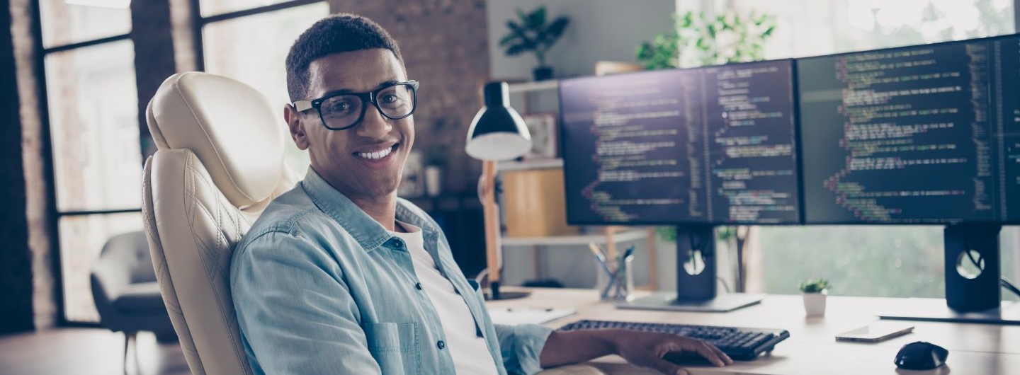 Python für Data Science and Machine Learning Weiterbildung: Ein junger Programmierer sitzt am PC und lächelt in die Kamera