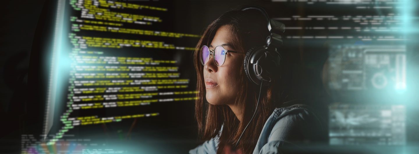 VBA Programmierung Weiterbildung: Eine junge Programmiererin sitzt mit Kopfhörern vor einem Bildschirm und arbeitet