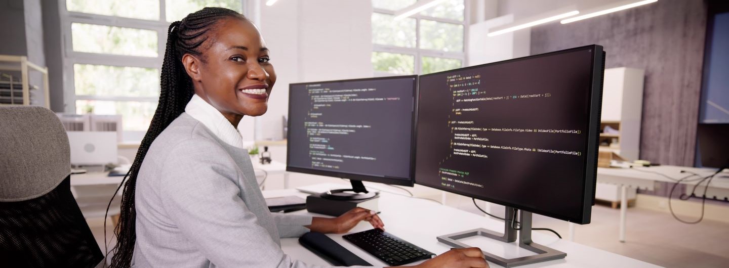 Web-Coding Weiterbildung: Eine junger Programmiererin sitzt am PC und lächelt in die Kamera